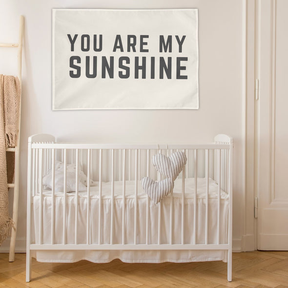 "you are my sunshine" wall flag hanging on the wall above a white crib in a nursery