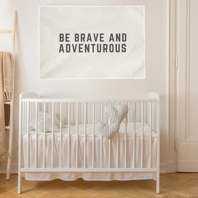 "be brave and adventurous" wall flag hanging above a crib in a nursery
