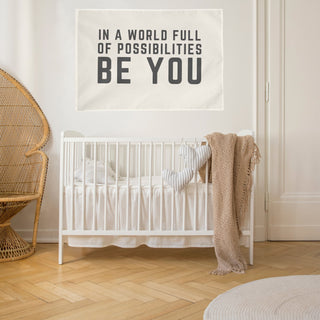 neutral baby nursery with "in a world of possibilities be you" wall flag hanging over the crib