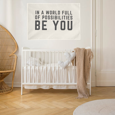 neutral baby nursery with "in a world of possibilities be you" wall flag hanging over the crib