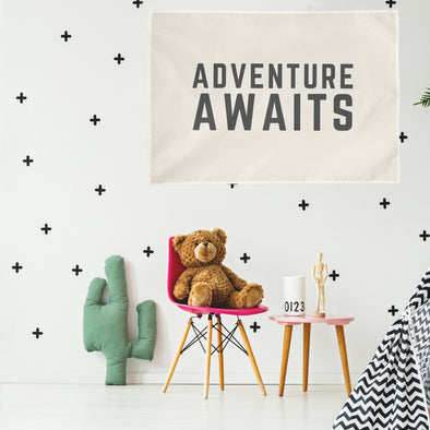 "adventure awaits" wall flag hanging above children's toys, table, and chair in their bedroom