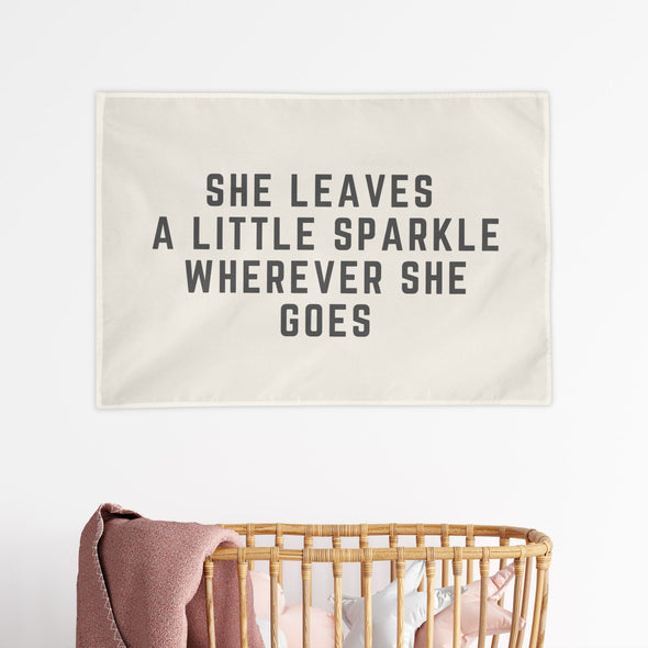 baby nursery with "she leaves a little sparkle wherever she goes" wall flag hanging above the crib