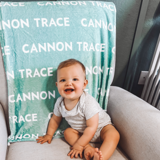 a smiling baby sitting on a chair in front of a blanket