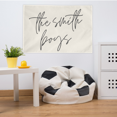 wall flag that reads "the smith boys" in a script font hanging above a soccer bean bag